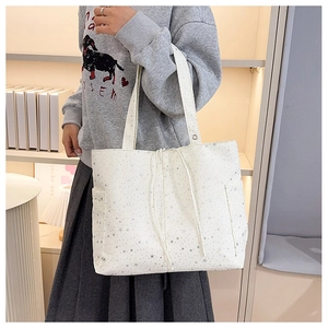 Detalle de un bolso tote de lona blanca con motivos de estrellas plateadas y cordón ajustable