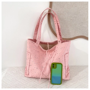Detalle de bolso tote de lona rosa con estrellas plateadas, bolsillos laterales y móvil para escala