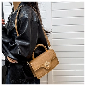 Close-up of tan crossbody bag with suede stitching and a gold flower-shaped metal clasp