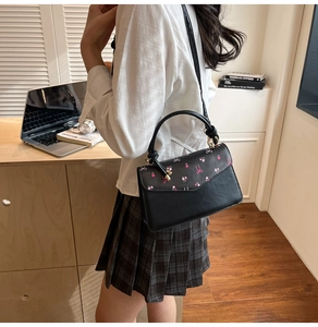 Detail view of black leather cherry print crossbody bag with metal ring handle and bow