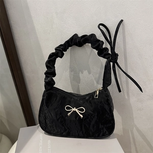 Chic black pleated handbag with golden metal bow detail on a stylish neutral background