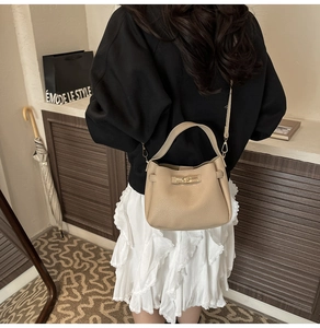Detail view of cream pebble leather bucket bag with gold twist lock and shoulder strap