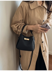 Close-up of black lychee grain leather bucket bag with gold lock on a stylish woman