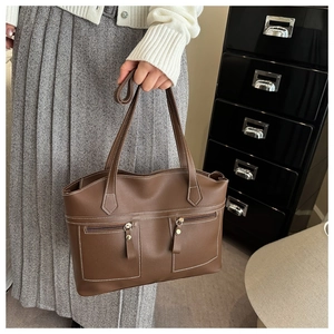 Detail of soft brown leather tote with white stitching and zipper pockets on a model