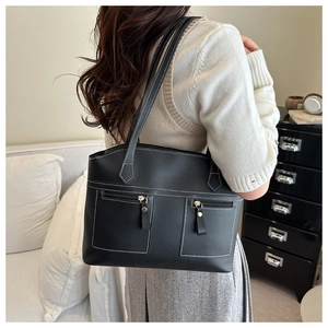 Close-up of black leather tote bag featuring contrast white stitching and dual zipper pockets