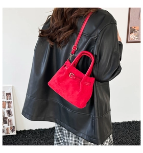 Detail view of red faux suede handbag with adjustable strap and leather buckle decor