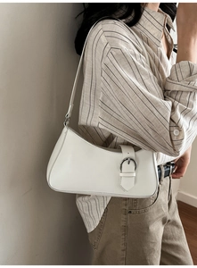 White leather baguette bag with silver buckle worn over the shoulder by a model