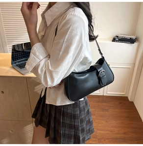 Side view of black faux leather baguette shoulder bag with silver buckle on a model