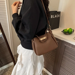 Brown lychee-grain leather tote bag with gold metal buckle shown on a stylish model