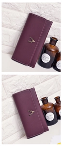 Vertical view of a burgundy long wallet with gold deer ornament on textured wall