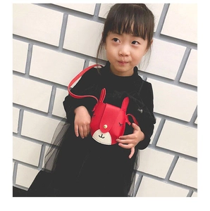 Toddler girl wearing a red and white cartoon deer crossbody bag against a brick wall