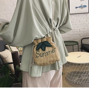 Dettaglio di una borsa a secchiello in paglia con ricamo a foglia verde e scritta Summer