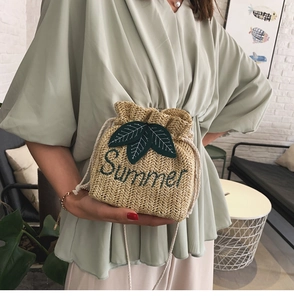 Dettaglio della borsa a secchiello in paglia con ricamo Summer e toppe a foglia da modella