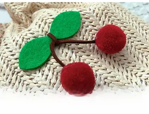 Dettaglio charm borsa ciliegia con pompon rossi e foglie di feltro su trama di paglia intrecciata