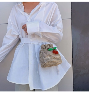Dettaglio borsa a secchiello in paglia intrecciata con coulisse bianca e ciliegie decorative
