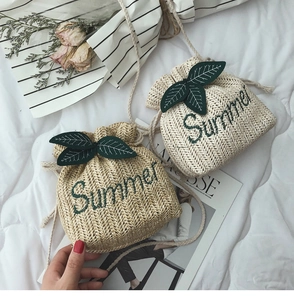 Dettaglio di borse a secchiello in paglia con ricamo Summer e foglie verdi decorative