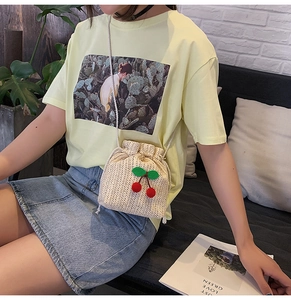 Dettaglio di una borsa a secchiello in paglia beige con ciliegie rosse e coulisse