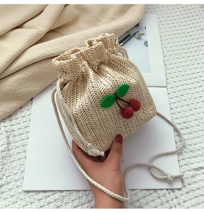 Dettaglio della borsa a secchiello in paglia con ciliegie 3D e coulisse in cotone bianco