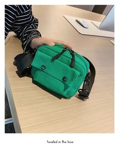 Detail of green canvas crossbody bag with black buckle pocket on wooden surface