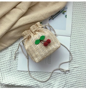 Dettaglio della borsa a secchiello in paglia con decorazioni a ciliegia e chiusura a cordoncino