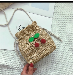 Dettaglio borsa a secchiello in paglia con ciliegie 3D e pratica chiusura a coulisse estiva