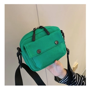 Detail of green canvas crossbody bag for kids featuring double zippers and front flap pocket