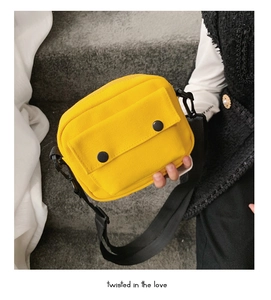 Close-up of bright yellow canvas crossbody bag featuring dual black button pockets