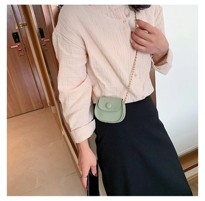 Close-up of light green mini saddle bag with gold chain strap on a female model