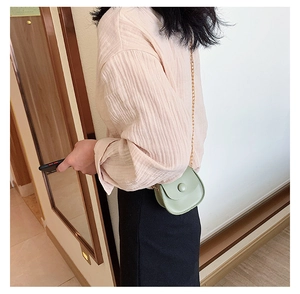 Detail of mint green mini crossbody bag with gold chain strap on pink shirt
