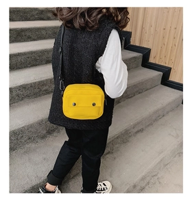 Front pocket detail of the yellow canvas crossbody bag featuring dual black button accents