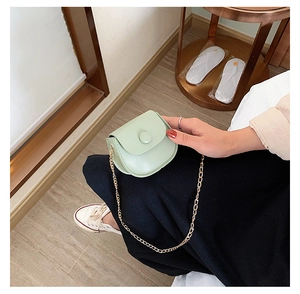 Detail of mint green mini saddle bag with gold chain strap held by a model
