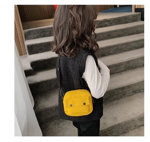 Detail of yellow canvas kids crossbody bag featuring adjustable black strap and front snaps