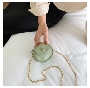 Detail of mint green mini round crossbody bag with gold chain strap on white bedding