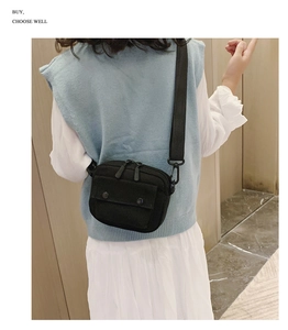 Detail view of small black canvas crossbody bag with double zippers and adjustable strap