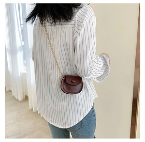 Detail of a dark brown mini round crossbody bag with a gold chain strap on a model