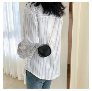 Mini black round crossbody bag with golden chain strap on model for stylish look