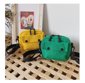 Detail view of canvas crossbody bags in yellow and green with front button pockets