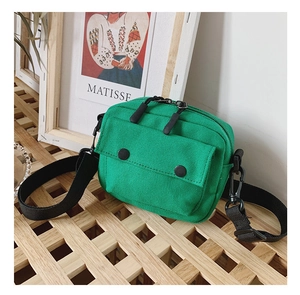 Detail of green canvas crossbody bag with adjustable strap on a minimalist wooden stand