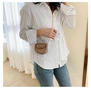 Detail of a mini khaki saddle bag with a fine gold chain on a striped shirt