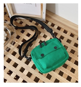 Detail shot of emerald green canvas bag with adjustable black strap on wooden surface