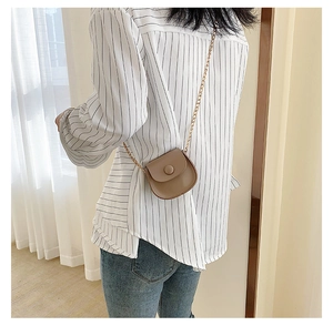 Girl wearing a light brown mini U-shaped crossbody bag with gold chain strap indoors