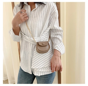 Detail shot of a khaki mini saddle bag with gold chain strap on a striped shirt model