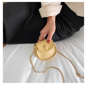 Detail of a light yellow mini crossbody bag with a gold chain strap and smooth texture