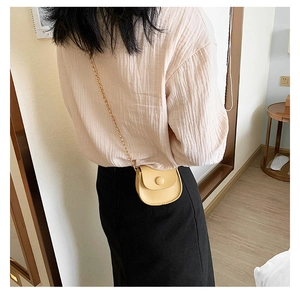 Detailed view of beige mini saddle crossbody bag with gold chain strap on model
