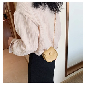 Detail of girl's pale yellow circular crossbody bag with gold chain and flap closure