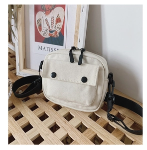Detail of off-white canvas crossbody bag with black zippers and adjustable strap