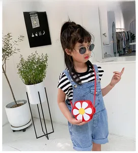 Close-up of red flower-shaped crossbody bag styled with denim overalls and striped shirt