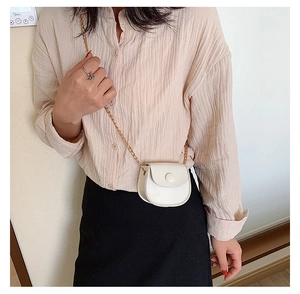 Close-up of white mini saddle bag with gold chain strap worn as a stylish crossbody