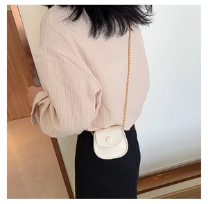 Detail of a mini cream white crossbody saddle bag with a golden chain strap on a model