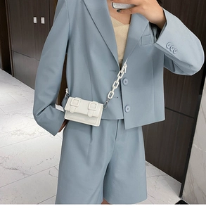 Close-up of white mini crossbody bag with chunky resin chain strap on a blue suit